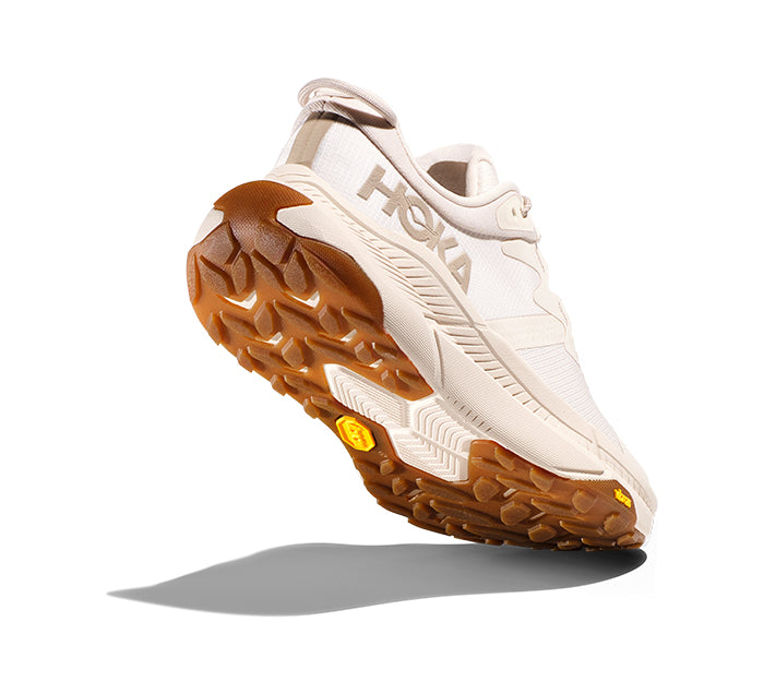 The HOKA Womens Transport Eggnog running shoe is shown from a low rear angle, highlighting its textured brown and white sole with visible tread, set against a white background with a shadow.
