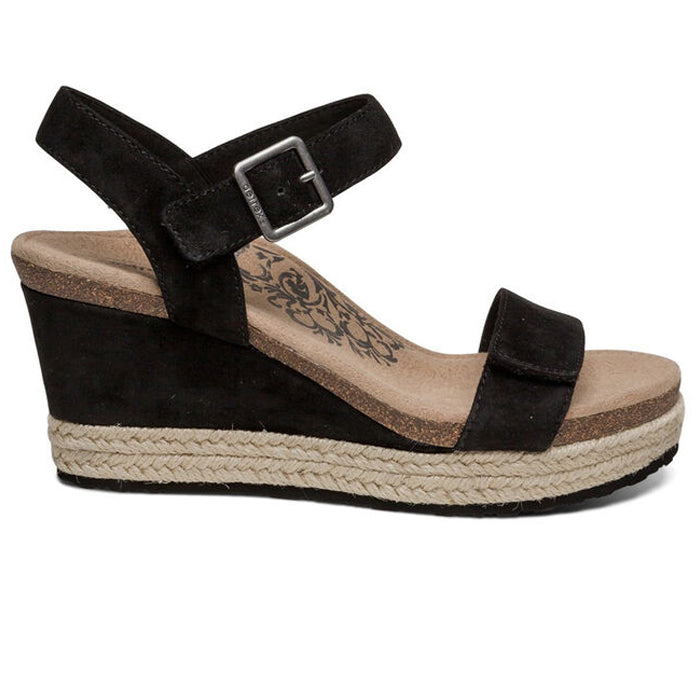 The Aetrex Womens Sydney Black by Aetrex is a black wedge sandal with an ankle strap, silver buckle, cork footbed with floral design, arch support for comfort, and a woven espadrille-style platform sole.
