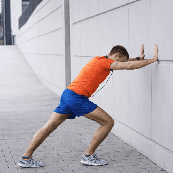 Man in athletic clothing performing a calf stretch by leaning against a wall