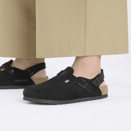 Person wearing black Birkenstock Buckley shearling-lined clogs with khaki trousers.