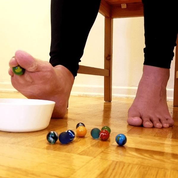 Bare feet picking up small colorful marbles with toes to place them into a white bowl