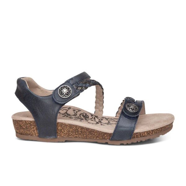 The Aetrex Womens Jillian Navy sandal features a navy blue open-toe design, decorative buttons, braided strap, low cork wedge heel, APMA Approved comfort, and a floral print on the beige insole.