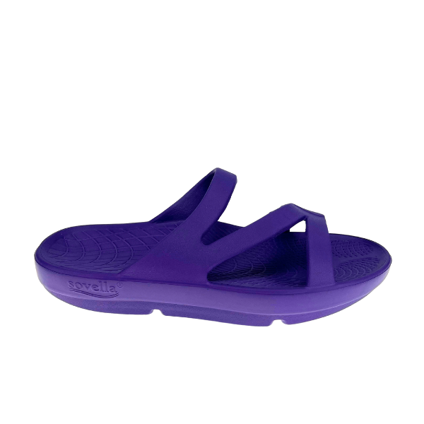 The Sovella Womens PF Slide Purple is a slip-on sandal with two Wide straps, a thick contoured sole, arch support, and textured footbed. These comfort recovery sandals display the SOVELLA brand name on the side.