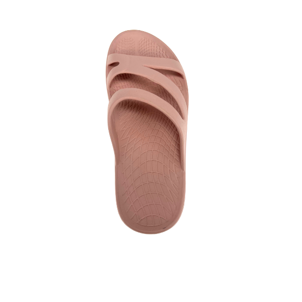 The Sovella Womens PF Slide Pink by SOVELLA is a light pink recovery sandal with arch support, a textured footbed, and two Wide overlapping straps, shown on a white background.