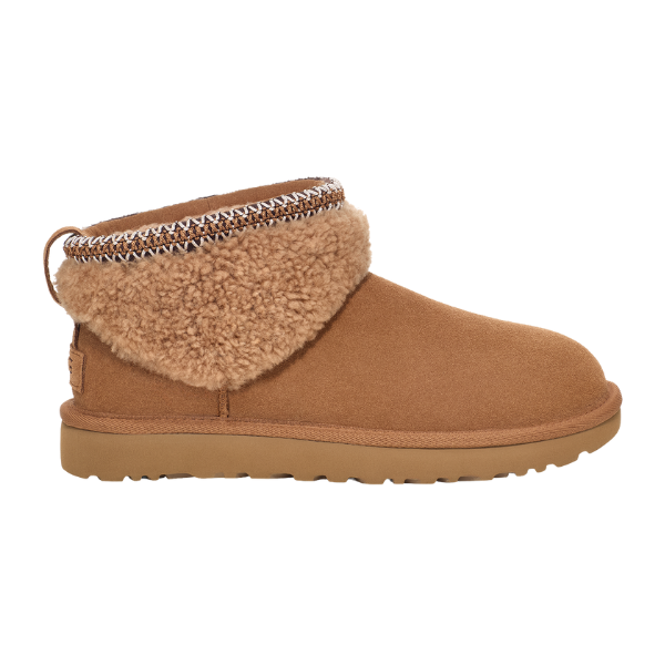 The UGG Women's Ultra Mini Maxi Chestnut is a brown suede ankle boot with a flat UGG Classic outsole, plush shearling lining, decorative ankle trim, and a pull tab at the heel for a cozy, casual look reminiscent of curly sheepskin boots.