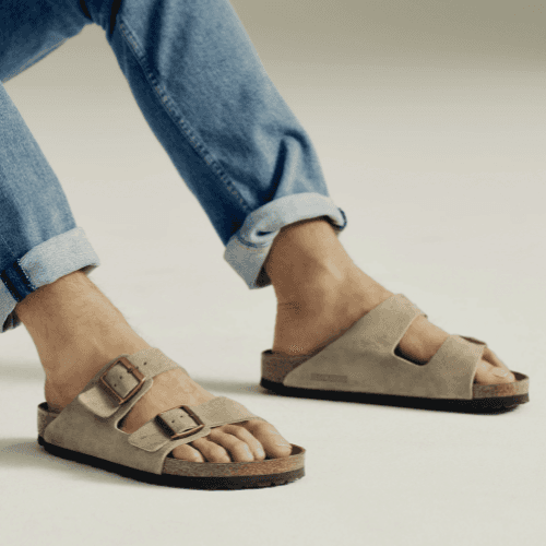 Person wearing taupe suede Birkenstock Arizona two-strap sandals with blue jeans.