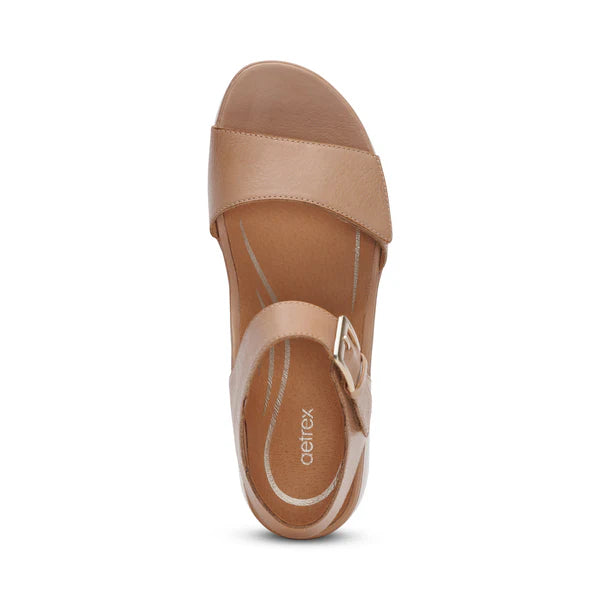 Top view of the Aetrex Women's Ariel Sand by AETREX WORLDWide INC, featuring tan leather, a wide front strap, ankle strap with gold buckle, and cushioned insole. This elegant yet supportive wedge sandal is shown on a plain white background.