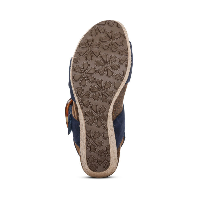 The image shows the brown sole with a textured floral pattern of the Aetrex Women's Ashley Espadrille Wedge Navy by AETREX WORLDWide INC. The dark blue leather upper features a side strap and buckle.