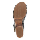 The image shows the bottom view of the Dansko Womens Alanna Black sandal by DANSKO, featuring a black upper and brown rubber sole with wavy tread for grip, designed for comfort and foot pain relief.