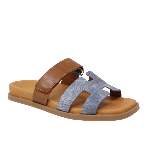 The Django & Juliette Womens Nodette Denim/Tan flat sandal features a tan footbed, brown leather instep strap, grayish-blue H-shaped front strap, and a comfortable flat rubber sole.