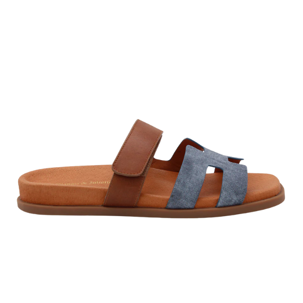 The Django & Juliette Womens Nodette Denim/Tan sandal features a flat sole, brown ankle strap, and blue denim-style front strap with chic cutouts—perfect for stylish comfort.