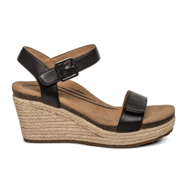 The Aetrex Womens Sydney Black Leather by Aetrex is a black ankle-strap wedge sandal with buckle, featuring a tan jute-wrapped platform and cushioned memory foam footbed for enhanced arch support.