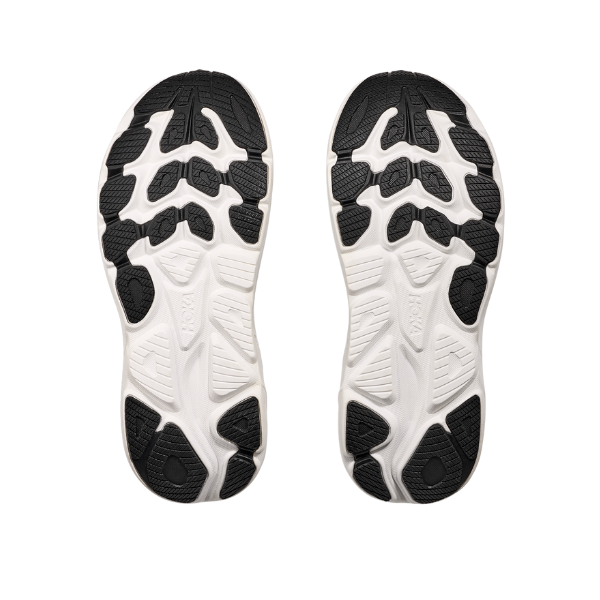 A pair of HOKA Mens Clifton 10 Wide Black/White running shoe soles are displayed side by side on a white background, highlighting their textured grip patterns and cushioned design.