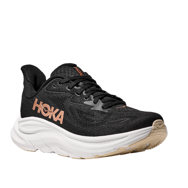 The Hoka Womens Clifton 10 Black/Gold is a cushioned running shoe with a thick white sole, tan tread, and bold peach HOKA lettering—ideal for everyday training.