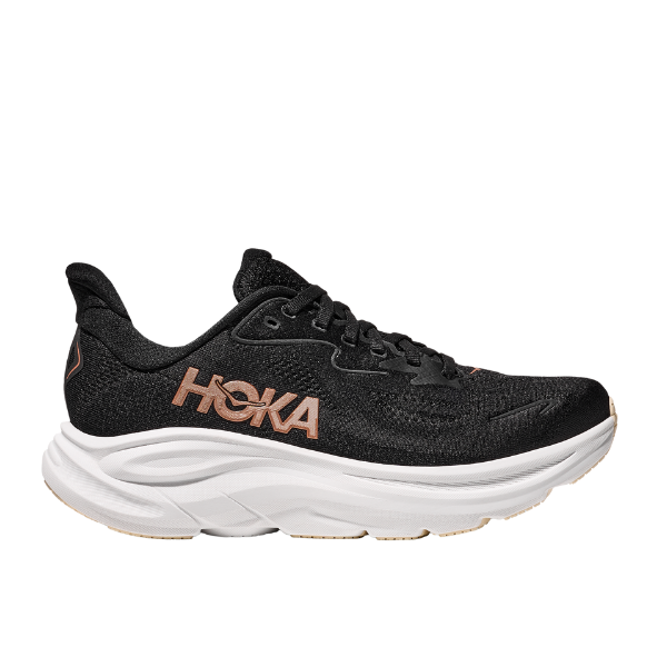 The HOKA Womens Clifton 10 in Black/Gold features a thick white sole and tan HOKA logo, offering cushioned comfort ideal for running; shown from the left against a white background.