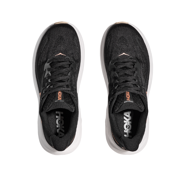 Top view of HOKA Womens Clifton 10 Black/Gold running shoes with white soles, side by side on a white background. These cushioned trainers combine style and comfort for every run.