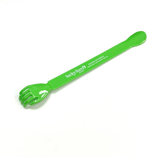 A green plastic shoehorn with a claw-like end, used for scratching, on a white background.