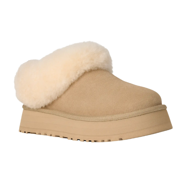 The UGG Women's Tazzelle Mustard Seed is a suede slip-on platform clog featuring a thick beige rubber sole, fluffy cream shearling trim, and cozy sheepskin lining for perfect comfort indoors or outdoors.