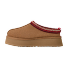 The UGG Women's Tazz II Chestnut is a tan slip-on shoe with a thick sole, red and cream decorative stitching, a red heel pull tab, and cozy sheepskin lining.