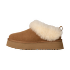 The UGG Women's Tazzelle Chestnut is a brown suede platform slipper featuring a thick flat rubber sole and plush cream fur lining around the opening.