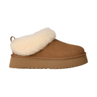 The UGG Women's Tazzelle Chestnut slipper features tan suede, a thick flat rubber sole, plush white shearling collar, closed toe, and heel pull tab for added comfort and style.
