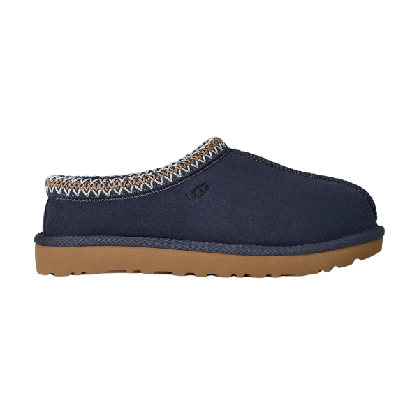 The UGG Women's Tasman II Dark Indigo slipper features a sheepskin upper in navy blue, brown rubber sole, and decorative ankle stitching, shown in side profile.