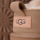 Close-up of the UGG Women's Classic Micro Sand boot, featuring the back heel tag with UGG logo, detailed stitching, plush wool lining, and a partial view of the sheepskin sole in the background.