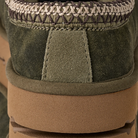 Close-up of the heel of UGG Men's Tasman Baxter Burnt Olive in green suede, with cream and brown criss-cross stitching and a thick brown rubber sole—highlights the signature style of UGG.
