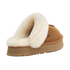 The UGG Women's Disquette Chestnut slipper features tan suede, a thick white fleece lining, and a brown rubber sole. Seen from a rear side angle, this cozy platform slip-on by UGG is ideal for indoor comfort.