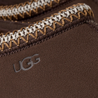 Close-up of the UGG Men's Tasman II Cocoa shoe, showcasing white and tan stitching, a soft suede upper with an embossed UGG logo, and plush sheepskin lining for comfort.