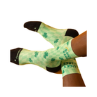 Person wearing FEETURES Elite Light Cushion Mini Crew – Lucky Vibes, green checkered socks with shamrocks, feet crossed.