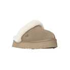 The UGG Womens Disquette Sand slipper features tan suede, signature sheepskin, a retro platform sole, and embossed UGG logo, photographed against a plain white background.