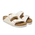BIRKENSTOCK Womens Arizona Birko-Flor Patent Offwhite/Eggshell sandals feature two adjustable buckled straps, a cork footbed, and a textured white sole, inspired by the classic Arizona design.