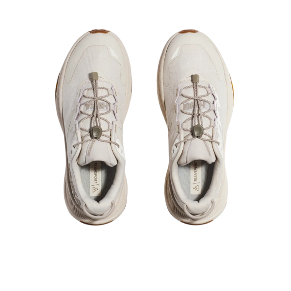 Top view of HOKA Womens Transport Wide Neutral sneakers in light beige, featuring elastic lace-up closures, brown rubber toe and heel accents, and a durable VIBRAM outsole by HOKA on a plain white background.