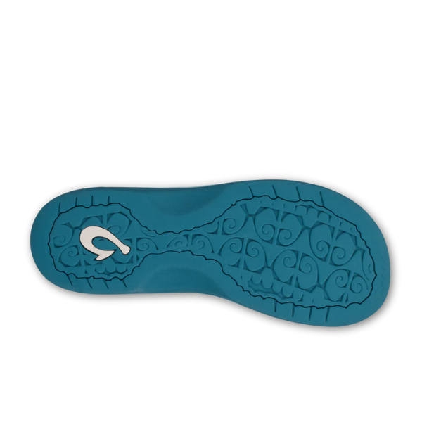 The OLUKAI Womens Ohana Misty Blue sandal features a teal textured sole with a white fishhook-shaped logo on the heel, highlighting its comfort footbed and water-resistant design, displayed against a white background.