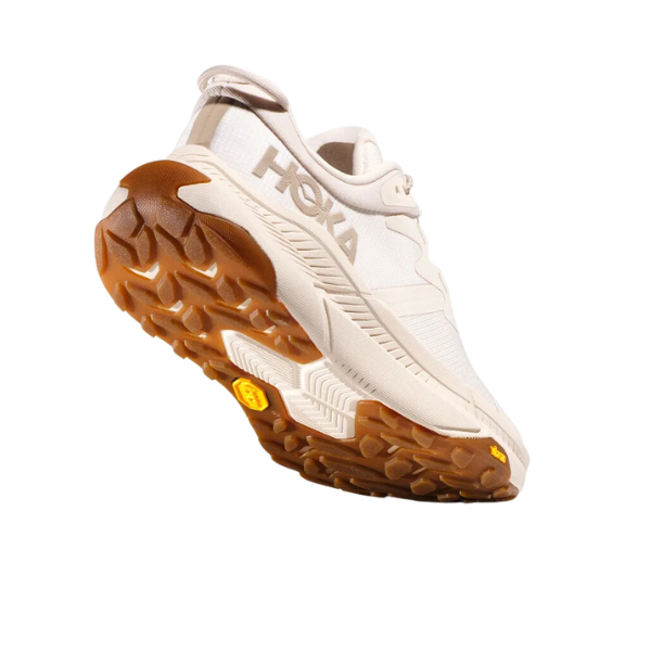 The HOKA Womens Transport Wide Neutral sneaker in beige is shown angled on a plain white background, featuring a thick, rugged VIBRAM outsole with textured tread and visible side branding.