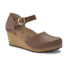 The BIRKENSTOCK Womens Mary Leather Cognac features a brown wedge heel, closed toe, ankle strap with buckle, and cork sole for comfort and style. Branding appears on the heel and insole for a signature finish.
