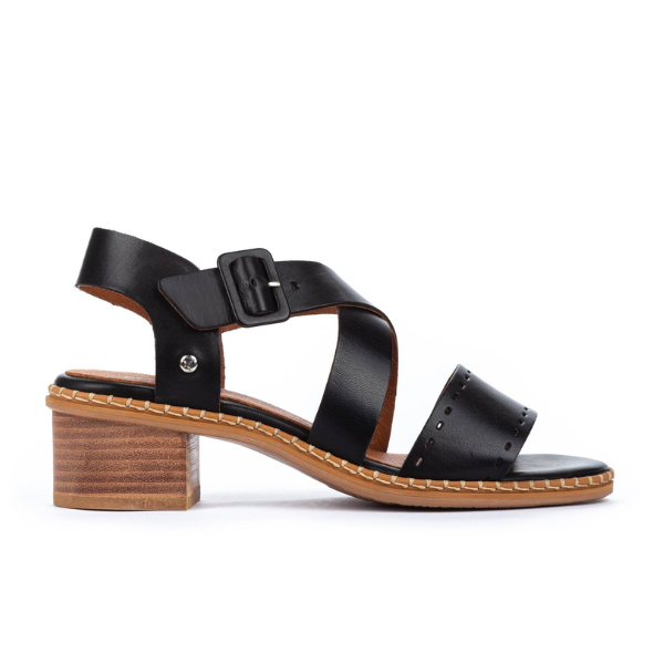 The Pikolinos Womens Blanes Heeled Sandals in black feature a punched leather design, thick toe strap, crisscross ankle straps with side buckle, chunky wooden heel, and white stitching along the sole for style. Brand: PIKOLINOS.