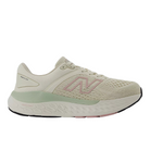 The New Balance Womens Fresh Foam X 1540v4 Wide Beige features a breathable mesh upper, light green Fresh Foam X midsole accent, pink N logo, and a thick cushioned sole with black and pink tread.