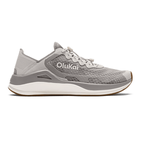 The OLUKAI Mens Ahi Ash/Sterling sneaker features a gray textured upper, white laces, and a white midsole, offering barefoot comfort. Shown from the side on a transparent background.