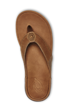The OLUKAI Mens Tuahine Toffee is a brown leather flip-flop sandal with a fabric thong strap, waterproof leather, and a stitched logo near the top, shown from above on a plain background.