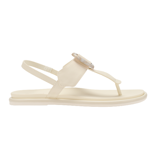 The OLUKAI Womens La‘i T–Bar in White Sand is a thong sandal with a thin ankle strap and large round accent on the upper strap. It features a matching flat sole designed for comfort, especially for those with foot pain.