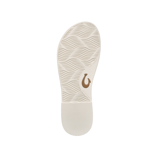 The OLUKAI Womens La‘i T–Bar White Sand sandal features a beige sole with a wavy texture, smooth heel, and brown hook-shaped logo by the arch, combining style and comfort, shown on a white background.