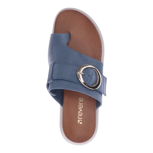 The Revere Womens Biscay Blue by REVERE is a blue leather slide sandal with a Wide strap, large silver buckle, brown contoured footbed, and revere branding on the insole. The strap partially covers the toes.
