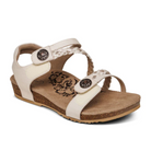 The Aetrex Womens Jillian Ivory by Aetrex features a beige open-toe design, low wedge heel, braided strap, adjustable closures with decorative buttons, floral cushioned insole, and an orthotic footbed for comfort.