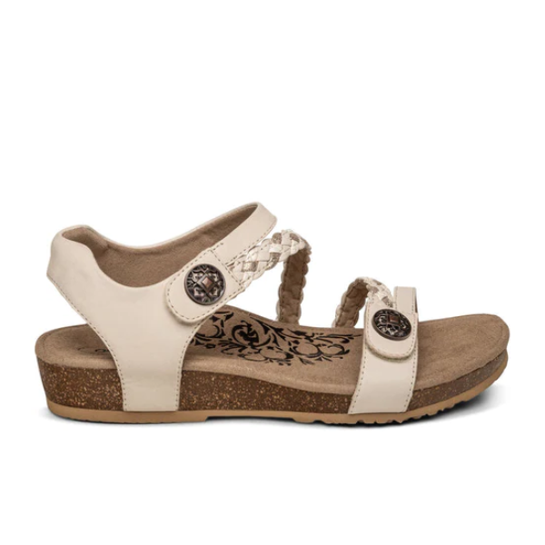 The Aetrex Womens Jillian Ivory sandal features two decorative metal buttons, braided strap detail, floral insole patterns, and a cork-textured sole with an orthotic footbed for comfort and an open toe design.