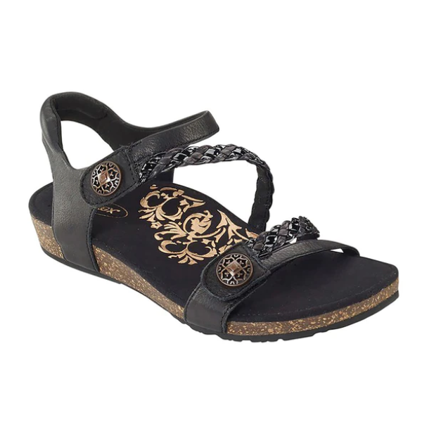 The Aetrex Womens Jillian Black sandal by Aetrex features two braided straps, decorative metal buttons, a cork-textured sole, a floral gold insole pattern, and an orthotic footbed for comfort.