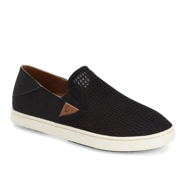 The OluKai Womens Pehuea Black is a slip-on sneaker with a mesh-textured upper, white sole, brown leather side accent, low-profile design, and an anatomical footbed for all-day comfort.