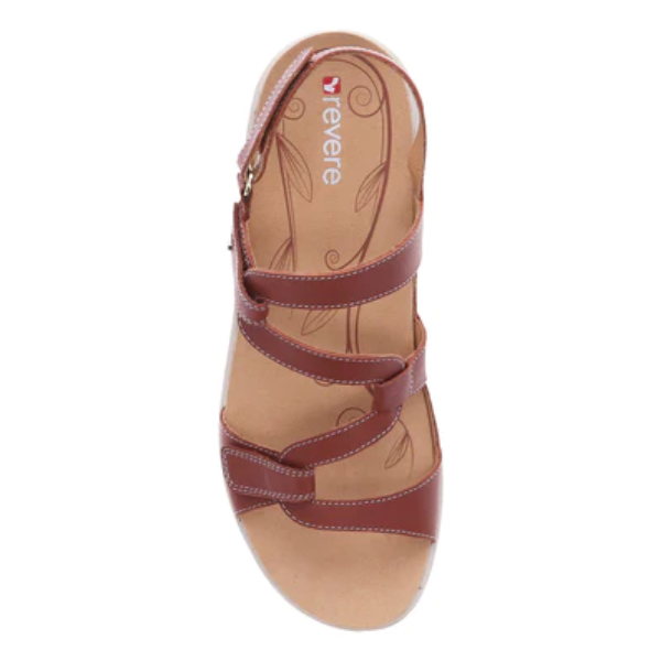 The Revere Womens Emerald Cognac sandal features luxe brown leather, three adjustable crossing straps with white stitching, a tan leaf-design insole, and REVERE branding near the heel.
