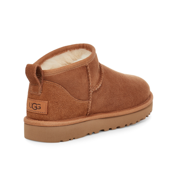 The UGG Womens Classic Ultra Mini Boot in Chestnut features a tan suede upper, low ankle cut, plush cream lining, stitched details, brown rubber sole, and signature heel logo patch. These iconic sheepskin boots provide foot pain relief.